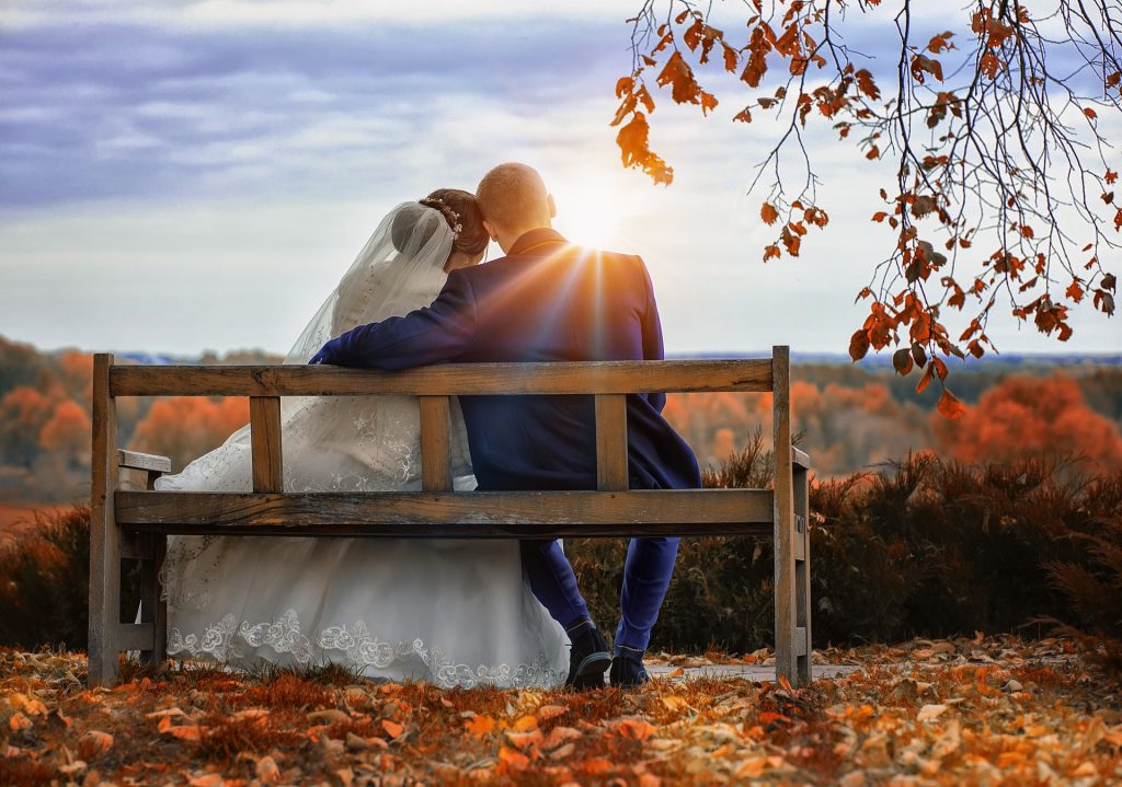 Brautpaar sitzt auf einer Bank im Herbstwald 