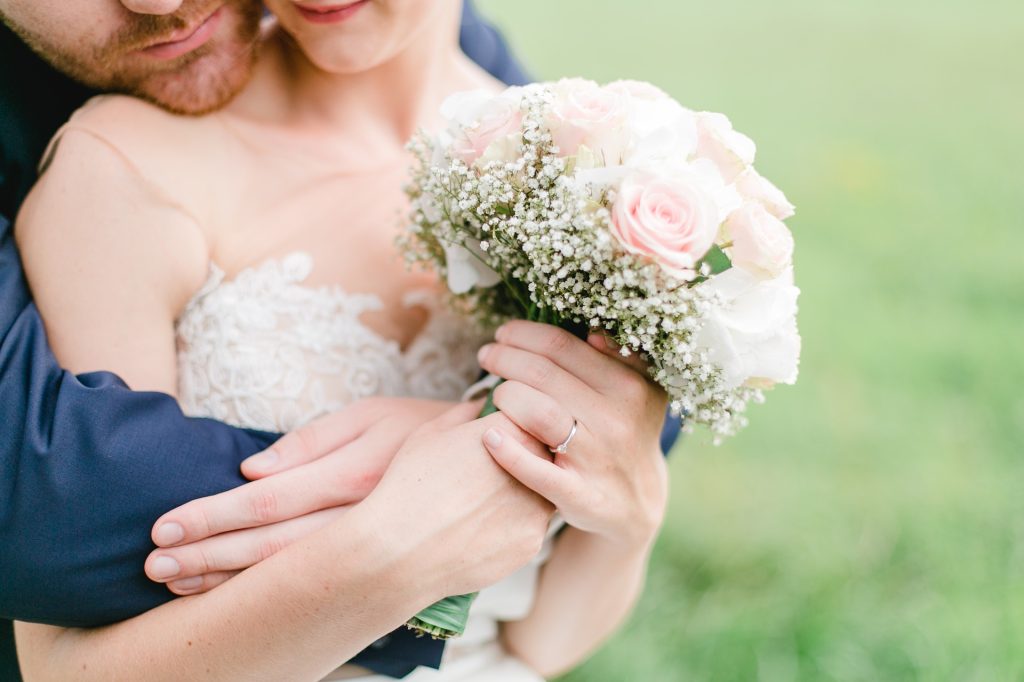 Sich umarmendes Brautpaar mit einem Brautstrauß bestückt mit rosafarbenen Rosen und Schleierkraut