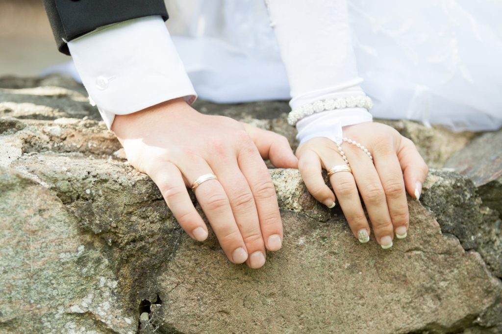 Brautpaar legt Hände mit goldenen Eheringen nebeneinander auf einen Steinfelsen