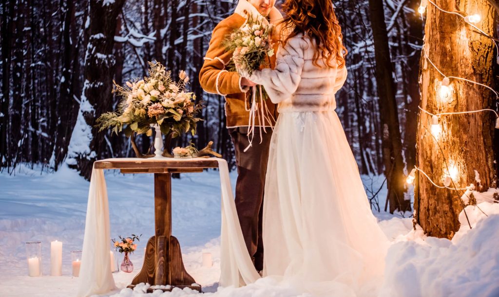Brautpaar feiert Winterhochzeit im Wald mit Kerzen und Lichterketten