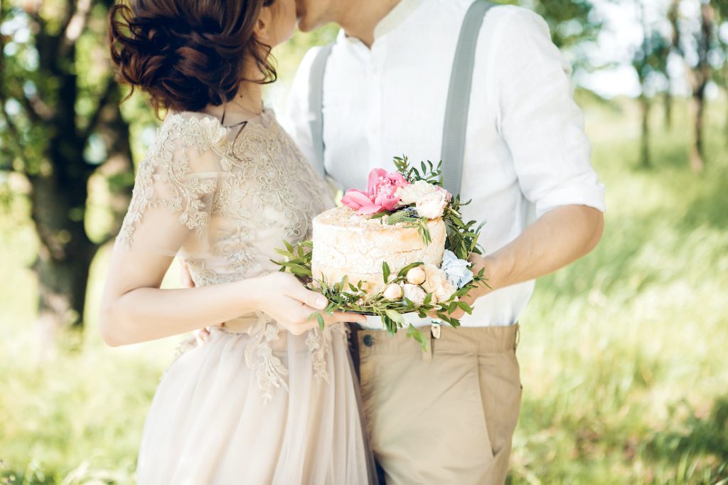 Perfekte Hochzeitstorte - Brautpaar hält mit Blumen bestückte Torte in den Händen