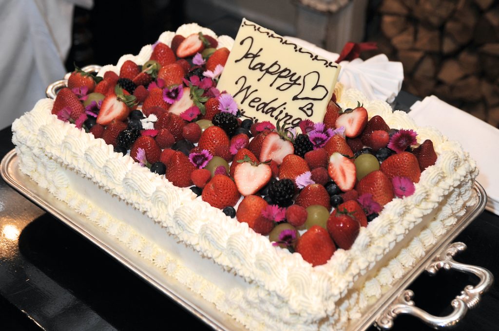 Die perfekte Hochzeitstorte - viereckig mit frischen Beeren und einer weißen Schokoladentafel mit der Aufschrift Happy Wedding