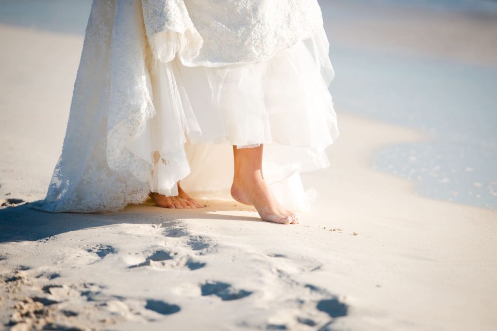 Destination Wedding: Braut geht barfuß durch den heißen Sand.