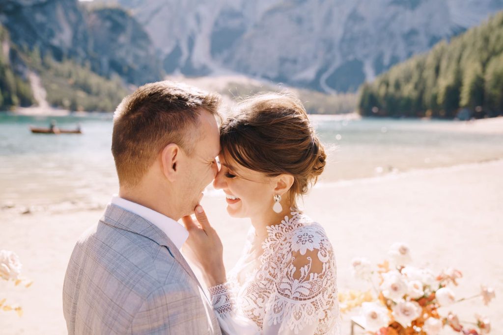 Brautpaar lächelt sich verliebt an vor einer traumhaften Kulisse mit einem Bergsee.