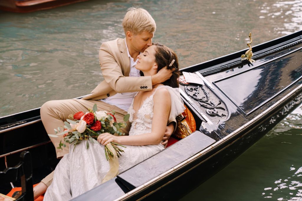 Destination Wedding: Brautpaar sitzt in einer Gondel. Dabei lehnt die Braut am Bräutigam und er gibt ihr einen sanften Kuss auf die Stirn.