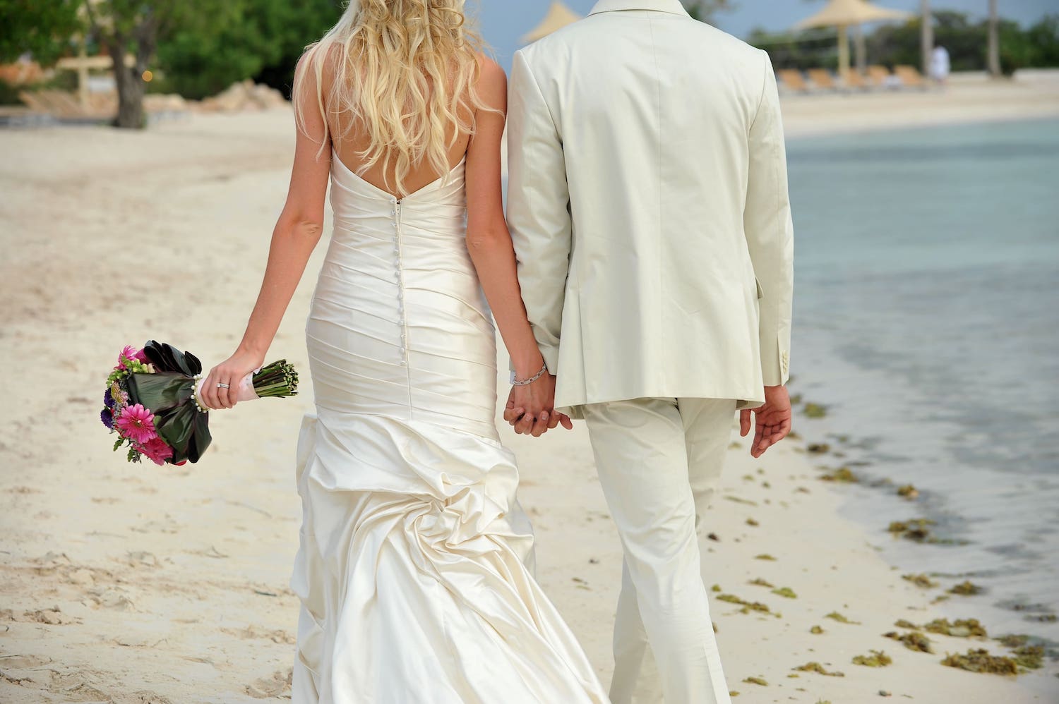 Destination Wedding: Brautpaar geht Hand in Hand am weißen Stand entlang