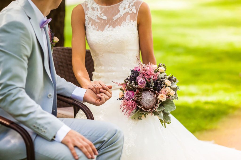 Brautpaar sitzt Hand in Hand auf einer Bank